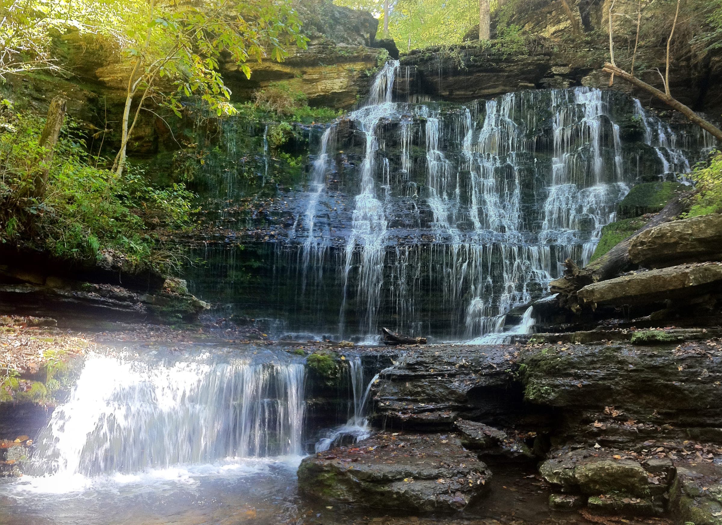 Machine Falls fanning roughly 60 feet down a wide, layered rock face into a shallow pool, seen from the creek at its base