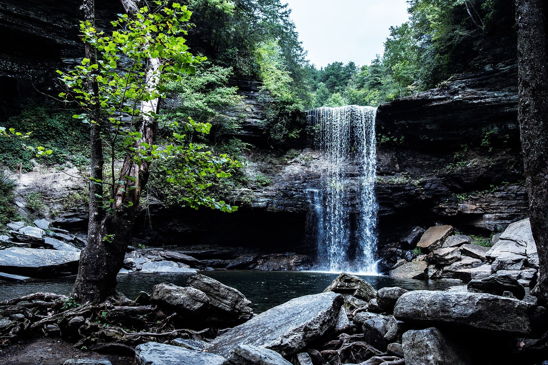 Lower Greeter Falls pouring off an overhanging ledge into a boulder-ringed pool in the gorge